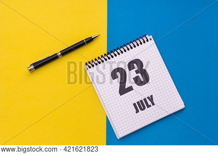July 23th. Day 23 Of Month, Calendar Date. Notebook With A Spiral And Pen Lies On A Yellow-blue Back