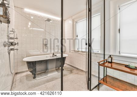 Glass Wall In Modern White Bathroom With Black Soaker Tub And Small Wooden Table At Window