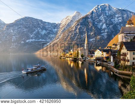 View Of Beautiful Hallstatt Lake And Famous Church During Morning Sunrise In Early Spring, Tour Boat