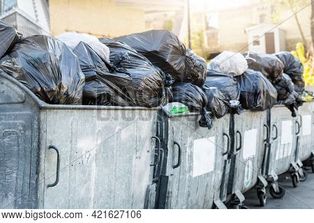 Rows Of Many Big Metal Overloaded Dumpster Cans Full Of Black Plastic Trash Litter Bags Near Residen
