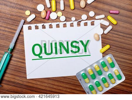 On A Wooden Table, A Syringe, Pills And A Sheet Of Paper With The Inscription Quinsy. Medical Concep
