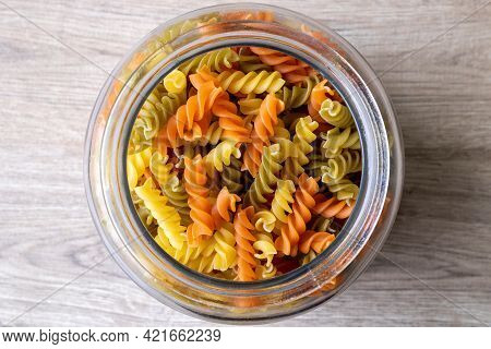 A Top Down Portrait Of A Glass Pot, Jar Or Bowl Full Of Spirelli In Three Different Colors. The Unco