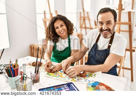 Two middle age students smiling happy modeling clay sitting on the table at art school.