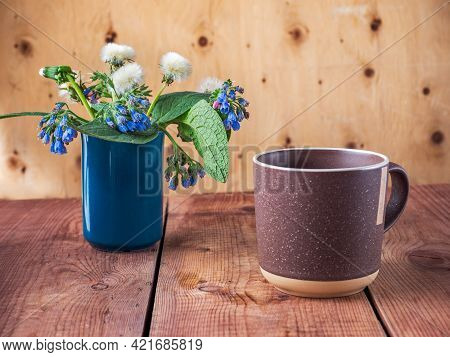 A Cup Of Morning Waffle In A Large Brown Mug And A Spring Bouquet, Dandelions And Blue Symphytum Cau