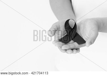 Hand Holding Black Ribbon On White Background With Copy Space, Symbol Of Skin Cancer Awareness Month