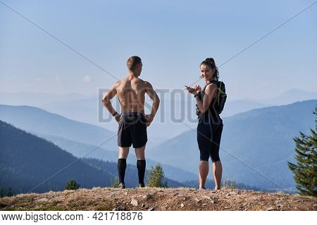 Back View Couple Of Hikers Standing On Rocky Top Of One Of Mountain Hills. Man Putting Hands Waist A