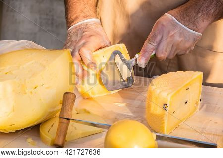 Shopkeeper's Hands Cutting A Head Of Cheese