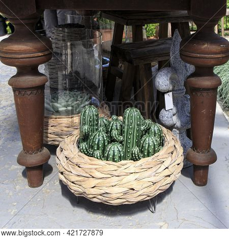 Wicker Basket With Ceramic Green Cactus Figurines Under The Table. Planter With Festuca Gautieri Ami