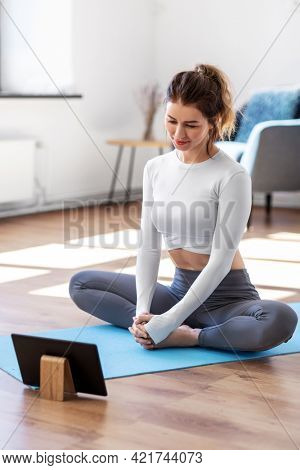 fitness, people and healthy lifestyle concept - young woman with tablet pc computer doing yoga at home