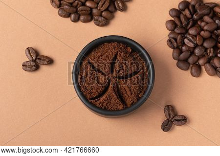 Ground Coffee In Black Bowl On Background Of Roasted Beans.coffee Background From Beans And  Blend C