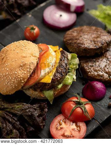 Juicy Hamburger And Ingredients For Its Preparation On Black Cutting Board. Sesame Bun With Tomato, 