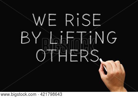 Hand Writing We Rise By Lifting Others With Chalk On Blackboard. Teamwork, Leadership, Altruism, Or 