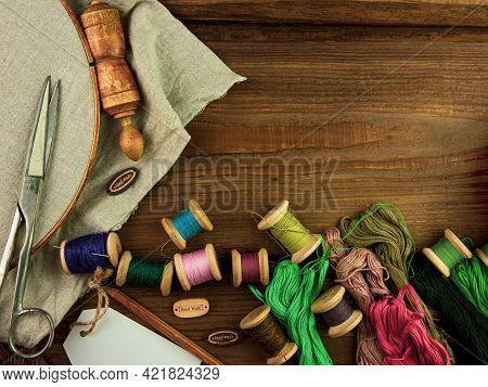 Embroidery Needlework Background With Linen In Hoop. Colorful Floss Thread, Scissors, Card Tag In Fe