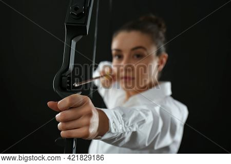 Businesswoman With Bow And Arrow Practicing Archery Against Black Background, Focus On Hand