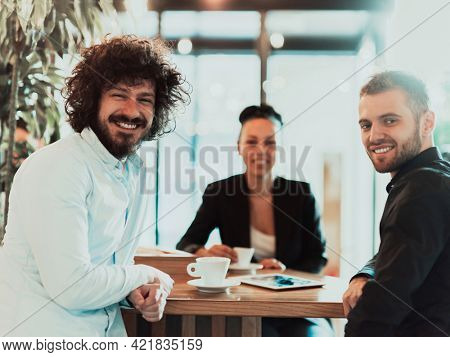 A group of business people on a coffee break use laptops, tablets and smartphones while discussing new business projects. 