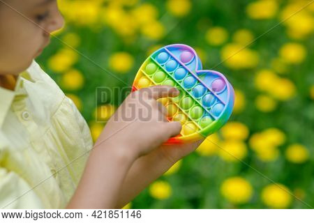 The Girl Is Holding A Colorful Game Of Poppit In Her Hands. Popular Pop Toy Of Rainbow Colors Close-