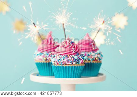 Three birthday cupcakes with pink frosting and party sparklers