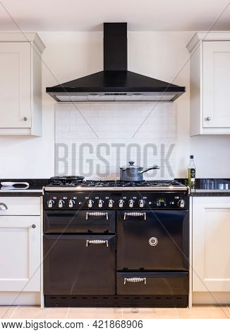 Black Enamel Oven Range Cooker With Chimney Hood In A Modern Kitchen With Shaker Style Painted Wood 