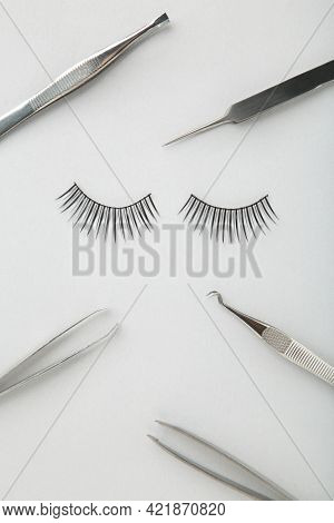 Set Of False Eyelashes Extencions On Grey Background With Tweezers. Minimalism. Top View