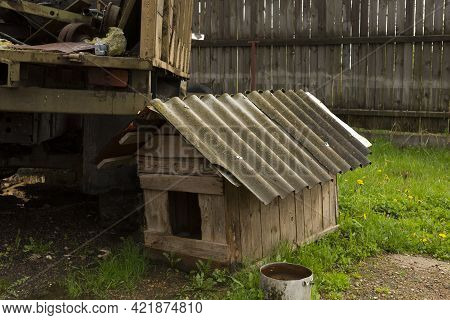 Wooden Old Doghouse In The Grass Near The House.one Old Empty Wooden Doghouse