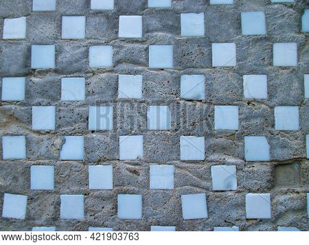 Background From An Old Gray Uneven Wall Of A Residential Building. With Blue Smalt Squares In A Chec