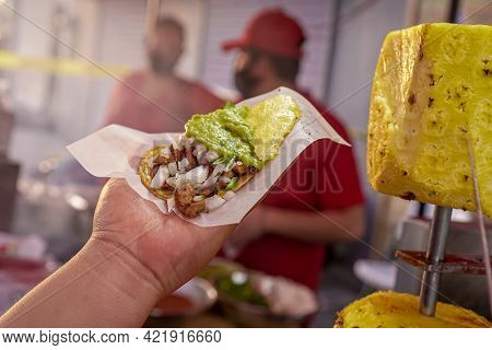 Exquisite Taco Of Adobada With Cilantro, Onion, Guacamole With A Slice Of Pineapple Held With A Hand