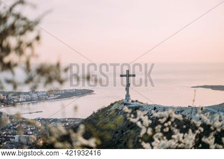 Gelendzhik, Russia, 03 May 2021: Orthodox Cross On Markotkh Ridge. A Flowering Tree In The Foregroun