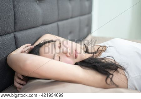 Asian Exhausted Girl Is Sleeping On The Bed, She Raises Hand Up On Her Head While Sleeping.