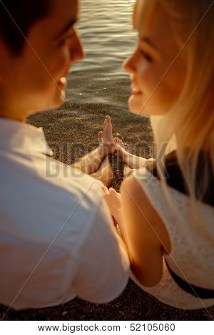 Couple Sitting And Watching One Another On The Beach At Sunrise