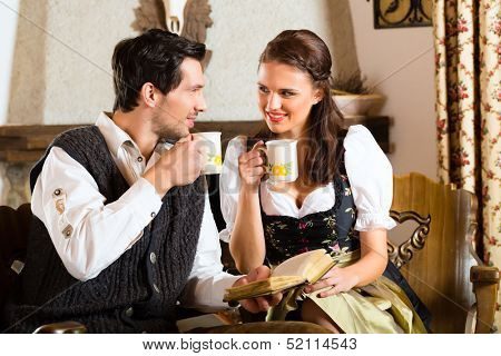 Couple in a traditional mountain hut with fireplace drinking coffee or tea