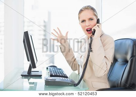 Angry blonde businesswoman screaming on the phone in bright office