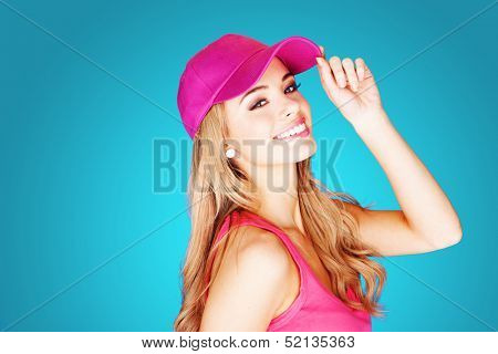 Vivacious beautiful blond woman in summer fashion wearing a trendy pink peak cap and top over a blue background