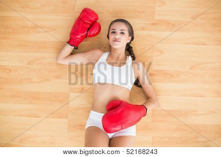 Sporty brunette woman having red boxing gloves on and lying on the floor