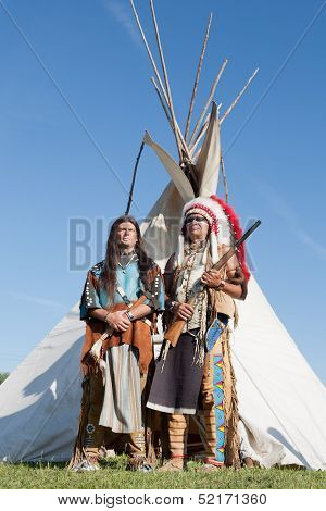 Two North American Indians stand near a wigwam