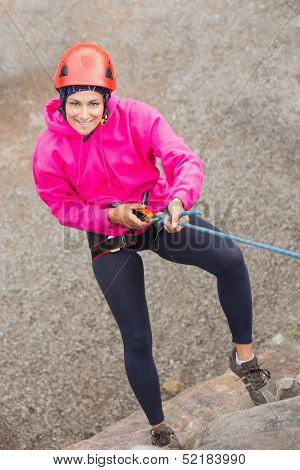 Happy girl abseiling down rock face looking up at camera