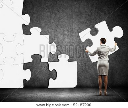 Image of businesswoman connecting elements of white puzzle