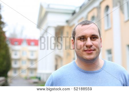 Outdoors portrait of happy young man in blue sweater in cloudy day