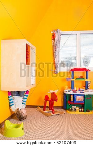 Little girl in children room sitting at the shelves upside down at inverted house