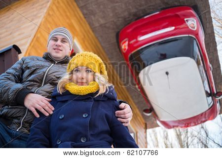 Couple against the inverted house with red car