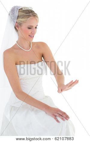 Smiling bride in off shoulder dress looking at wedding ring over white background