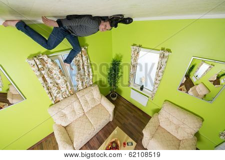 Man in jeans lying on the ceiling under the sofa without shoes and socks 