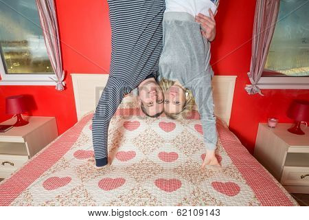 Couple in an embrace stand upside down on the bed in bedroom