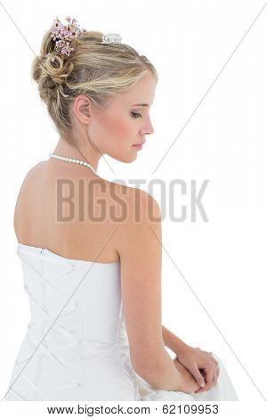 Beautiful young bride in off shoulder dress sitting against white background