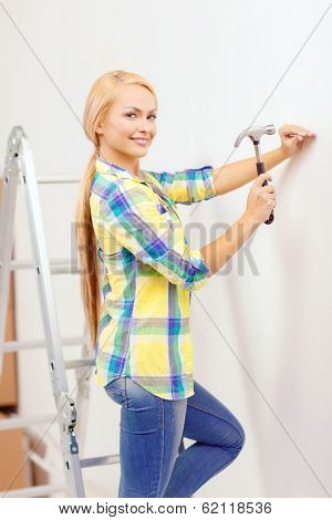 reapir, building and home renovation concept - smiling woman hammering nail in wall