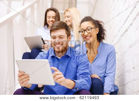 business, technology and startup concept - smiling creative team with tablet pc computer sitting on staircase