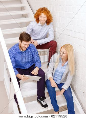 business, technology and startup concept - smiling creative team with tablet pc computer sitting on staircase