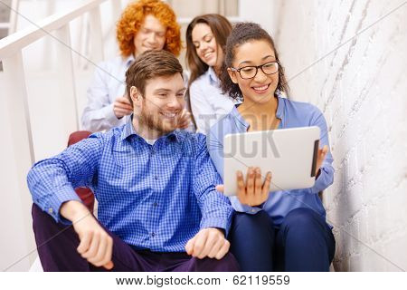 business, technology and startup concept - smiling creative team with tablet pc computer sitting on staircase