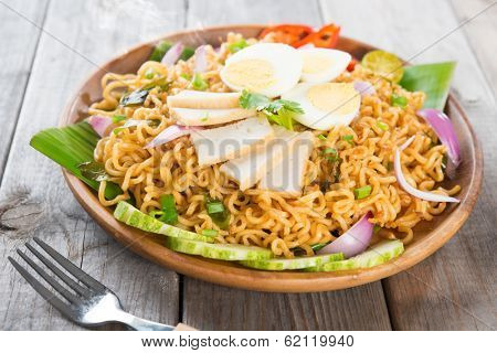 Dry Instant Noodle, Malaysian style maggi goreng mamak or spicy dry curry instant noodles. Asian cuisine, ready to serve on wooden dining table setting. Fresh hot with steamed smoke.