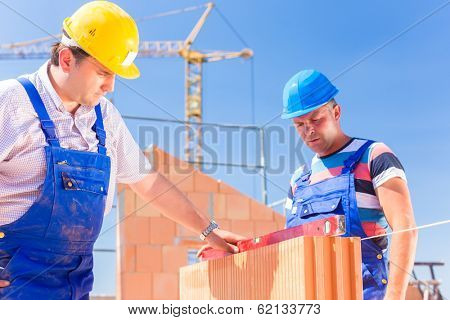 construction site worker or bricklayer with helmets controlling walls with a bubble level or building or laying or bricklaying wall on building 