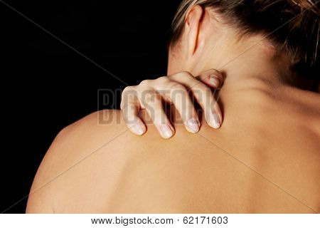 Nude, topless woman, scratching her neck. back view. On black background. 